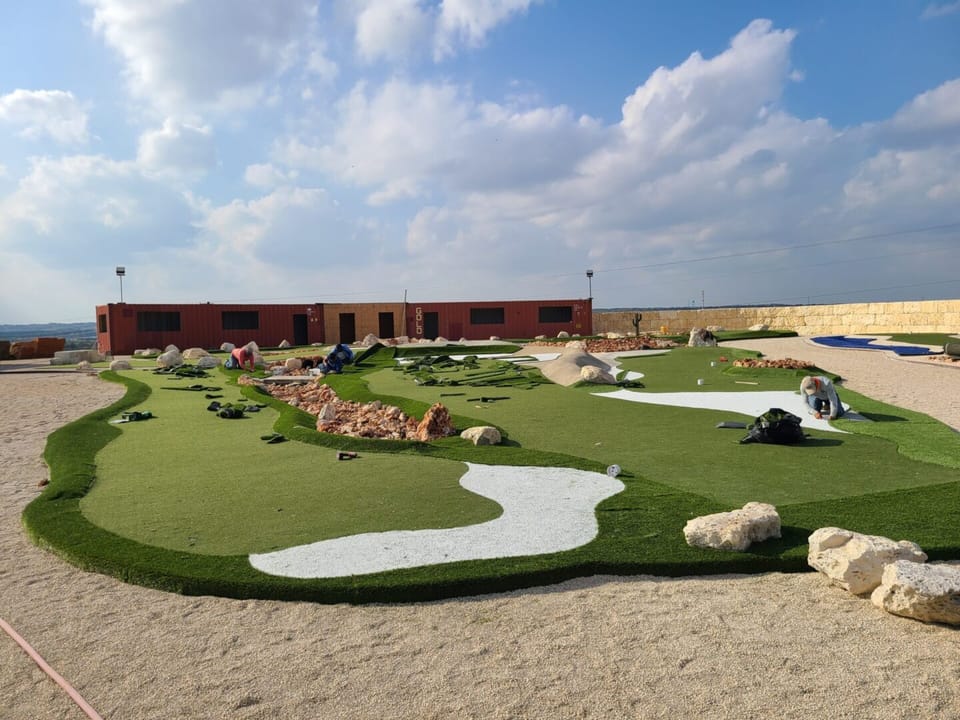Crew installing synthetic turf greens beside the clubhouse buildings.